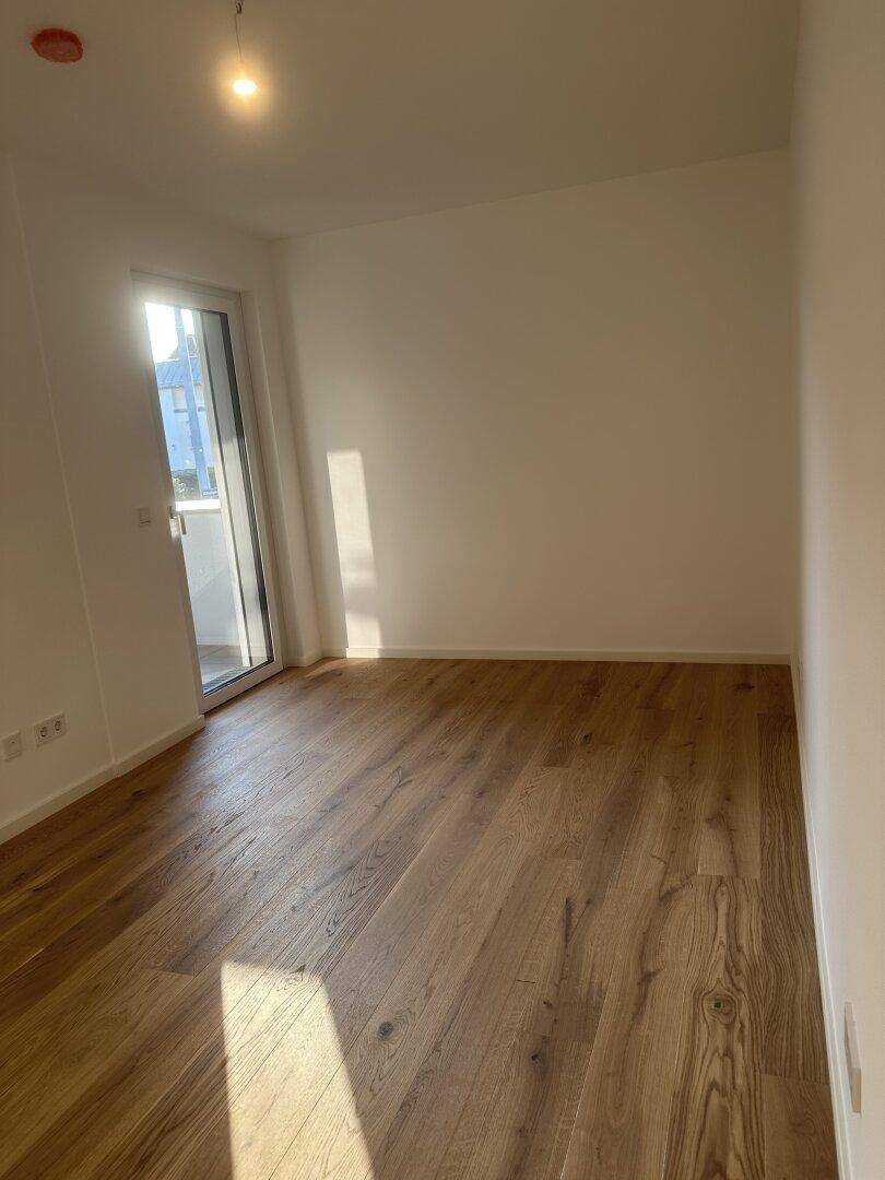 Lichtdurchflutetes Zimmer mit Holzboden und Zugang zu einem Außenbereich durch eine Glastür.