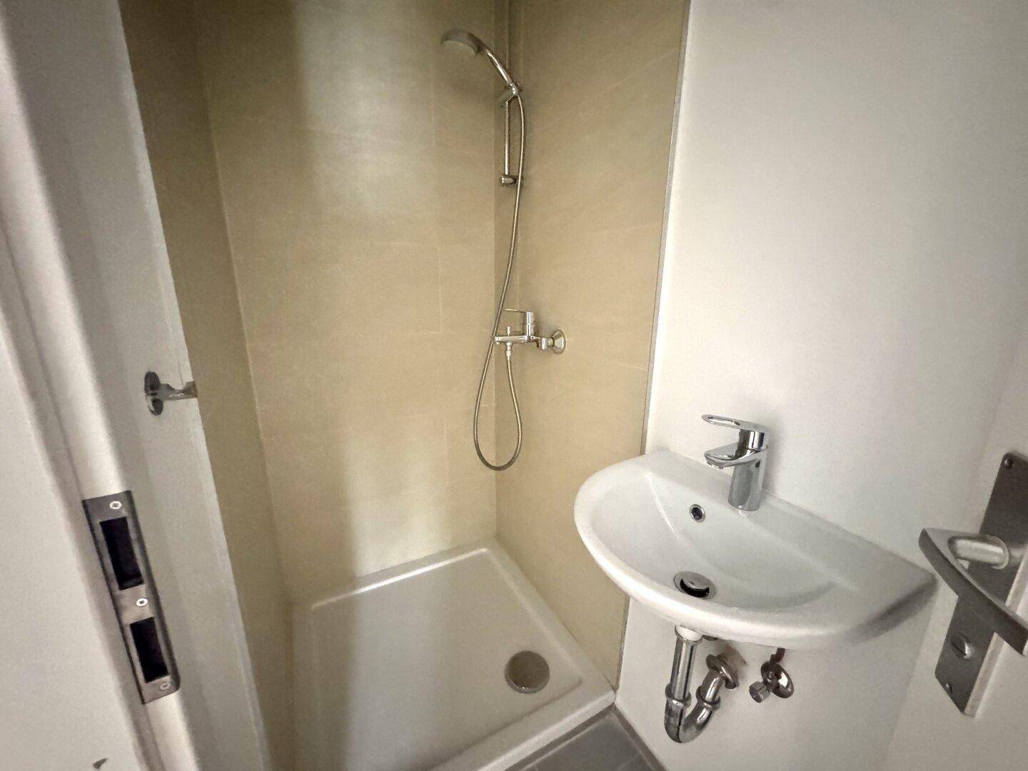 Kleines, funktionales Badezimmer mit Dusche und Waschbecken, hell gefliest und modern gestaltet.