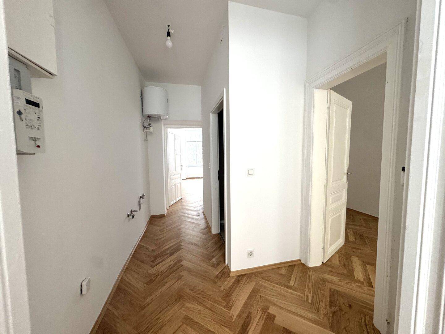 Heller Flur mit Fischgrätparkettboden und Zugang zu verschiedenen Zimmern der Wohnung.