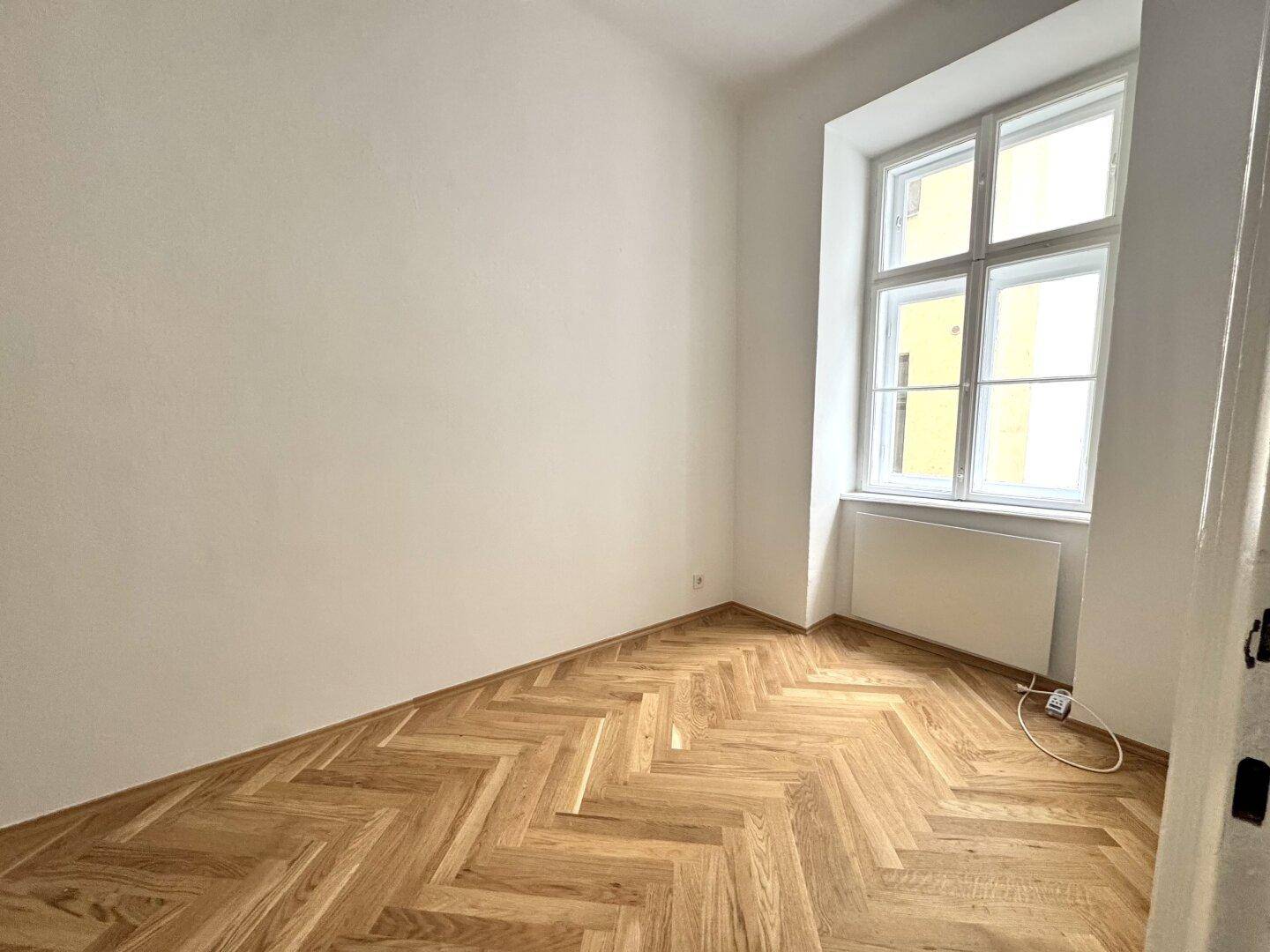 Gemütliches Zimmer mit Fischgrätparkett und einem großen Fenster, ideal als Schlaf- oder Arbeitszimmer.