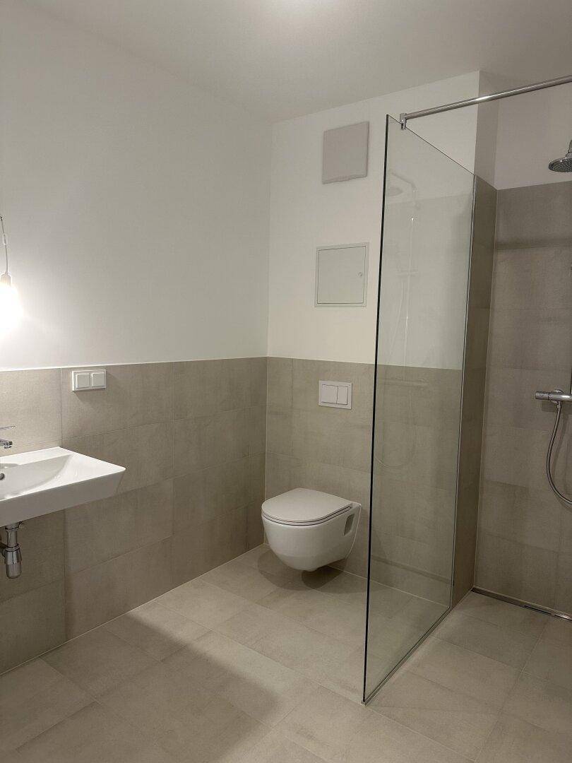 Modernes Badezimmer mit begehbarer Dusche, Wand-WC und hellen, großformatigen Fliesen.