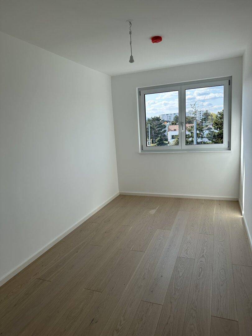 Leeres Zimmer mit hellem Holzboden und einem Fenster, das einen Blick auf die Umgebung bietet.