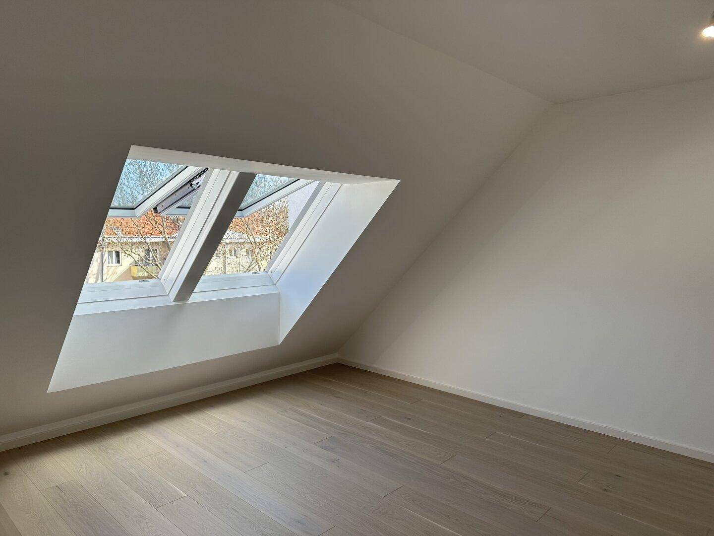 Helles Zimmer im Dachgeschoss mit Holzboden und schrägen Dachfenstern für viel Tageslicht.