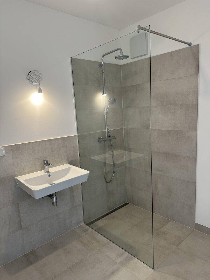Modernes Badezimmer mit ebenerdiger Dusche, Glaswand und einem eleganten Waschbecken.