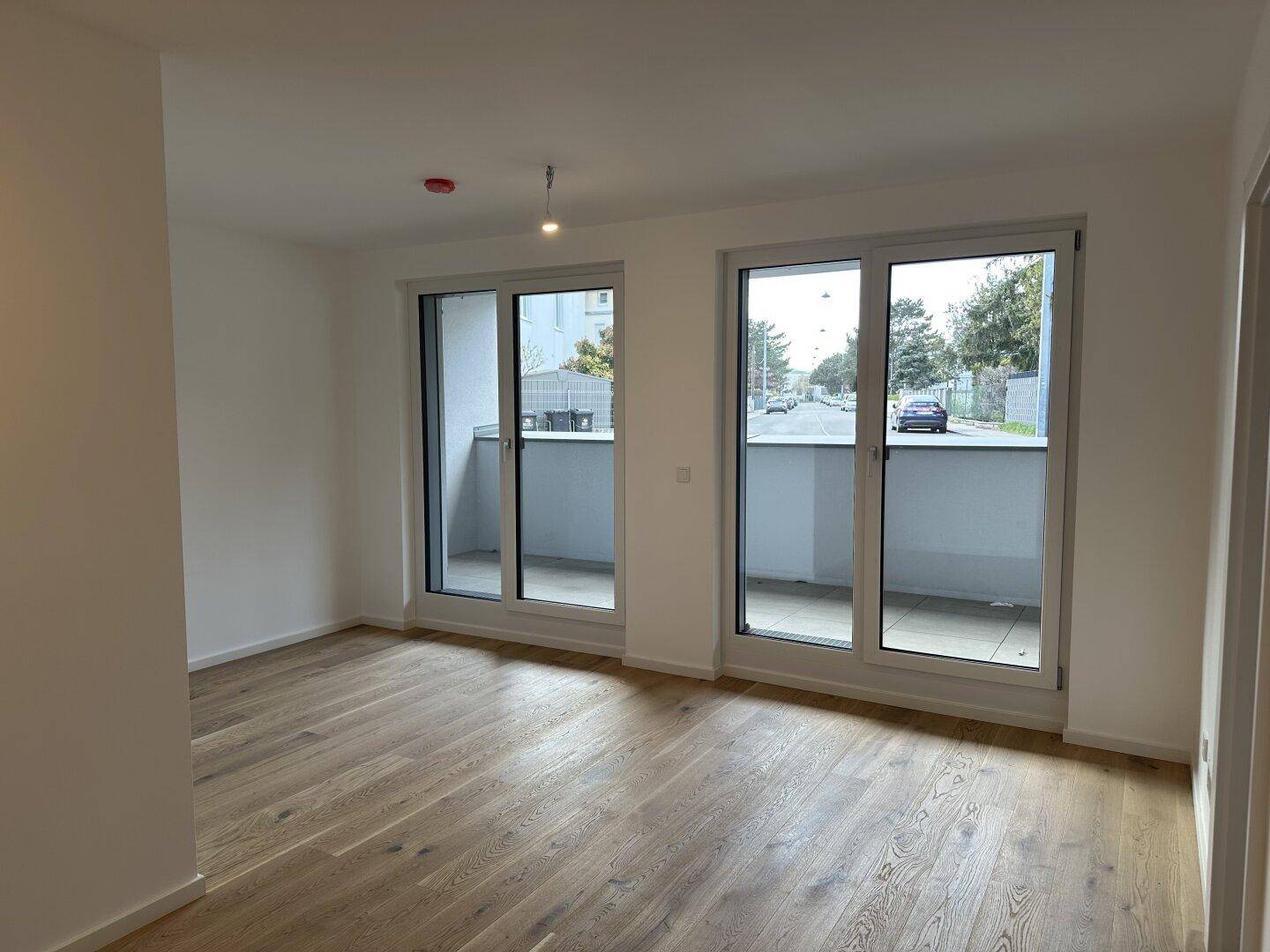 Geräumiger, heller Raum mit Holzdielenboden und zwei großen Fenstern zum Balkon.