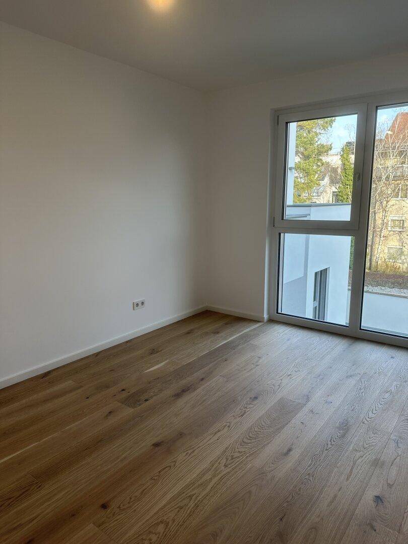 Helles Zimmer mit neuem Holzboden und großen Fenstern, die viel Tageslicht hereinlassen.