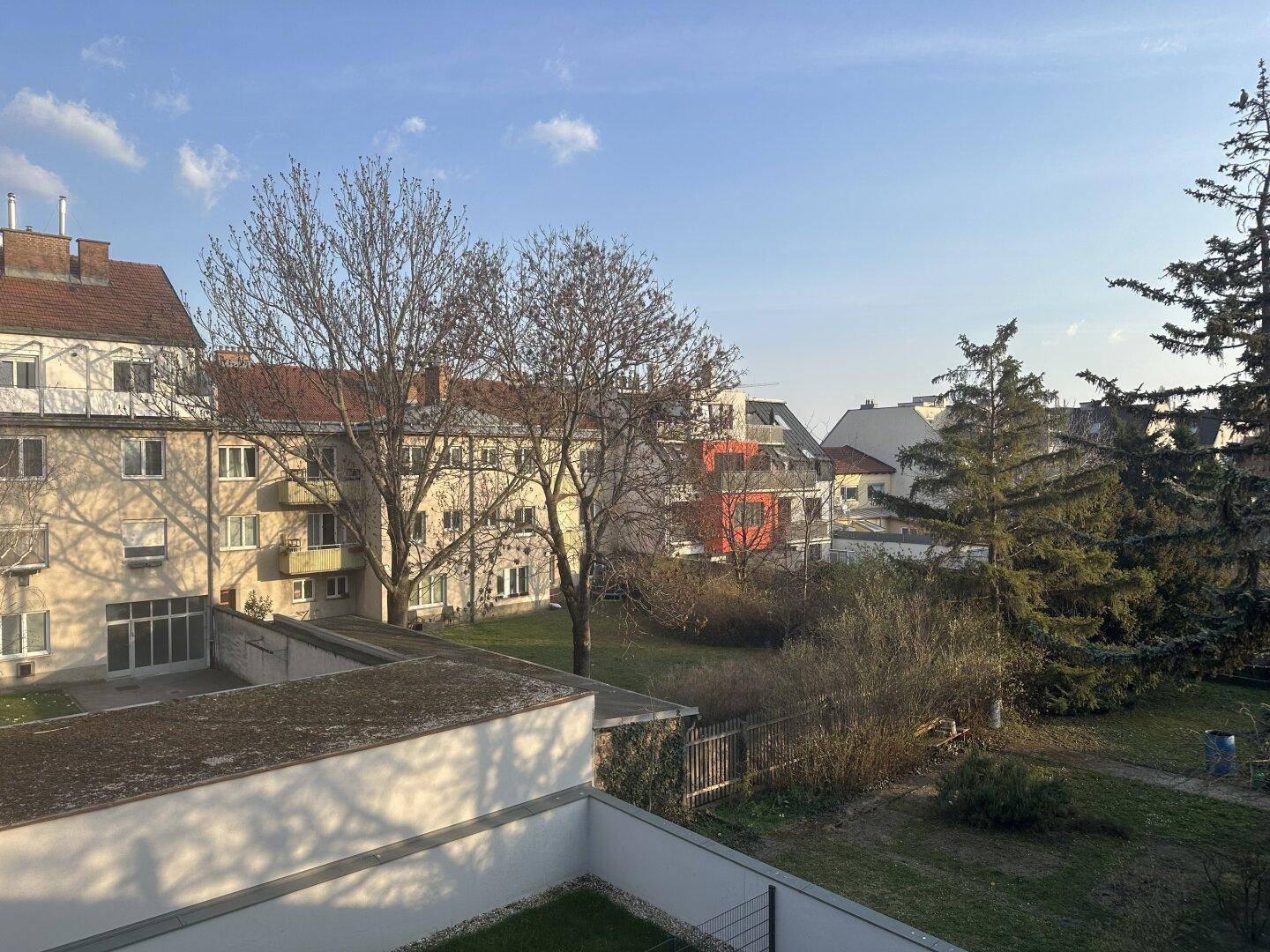 Weitläufiger Blick von einem Balkon auf eine grüne Umgebung mit Bäumen und Wohngebäuden.