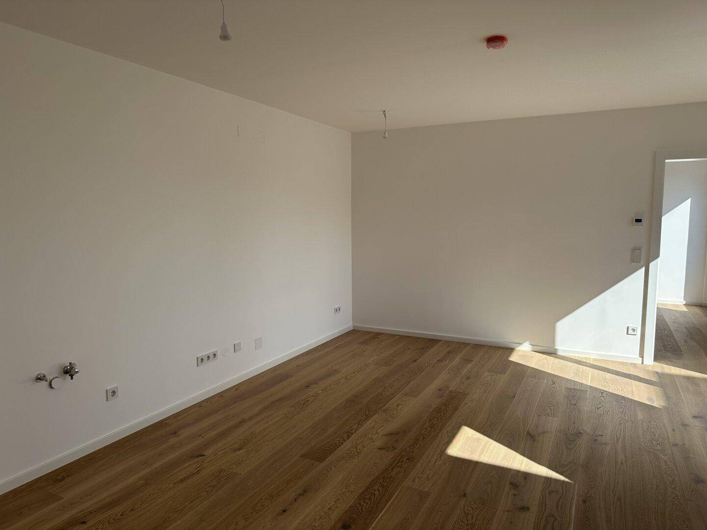 Heller Raum mit Holzboden und Anschlüssen für eine Küche, bereit für die Installation einer Einbauküche.