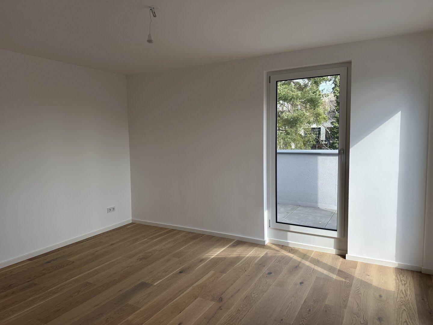 Lichtdurchfluteter Raum mit Holzboden und Zugang zu einem Außenbereich, ideal für Wohn- oder Esszimmer.