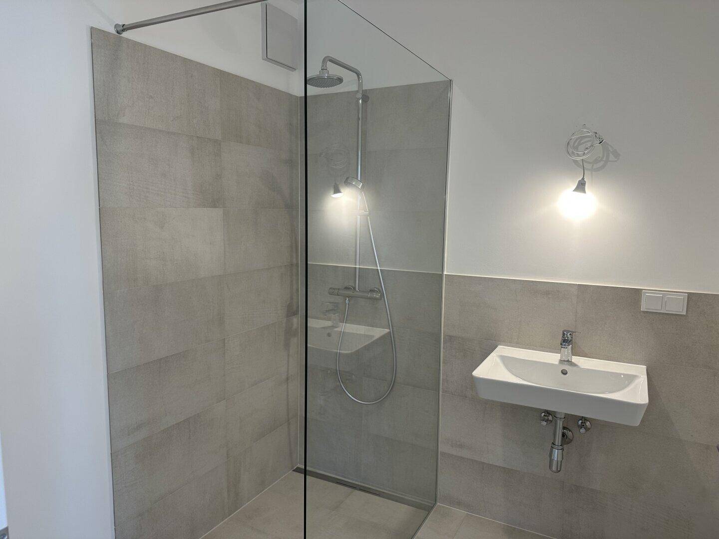 Modernes Badezimmer mit begehbarer Dusche, Regendusche und einem einzelnen Waschbecken, in hellen Grautönen gehalten.