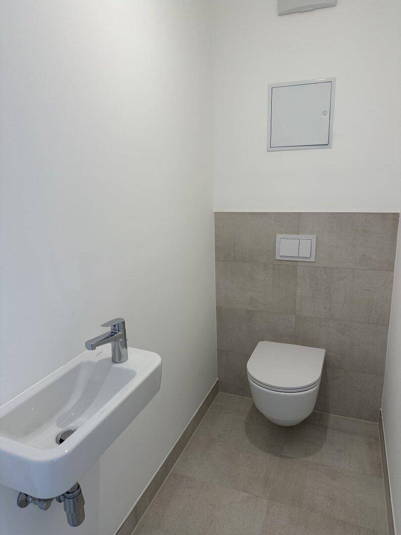 Modernes Gäste-WC mit wandhängender Toilette und kleinem Waschbecken, ausgestattet mit hellgrauen Fliesen.