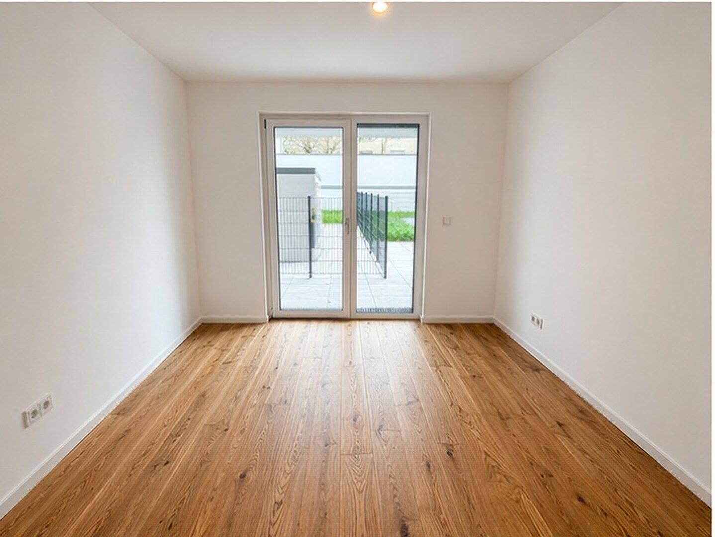 Geräumiges, helles Zimmer mit Holzboden und großen Fenstern zum Außenbereich.