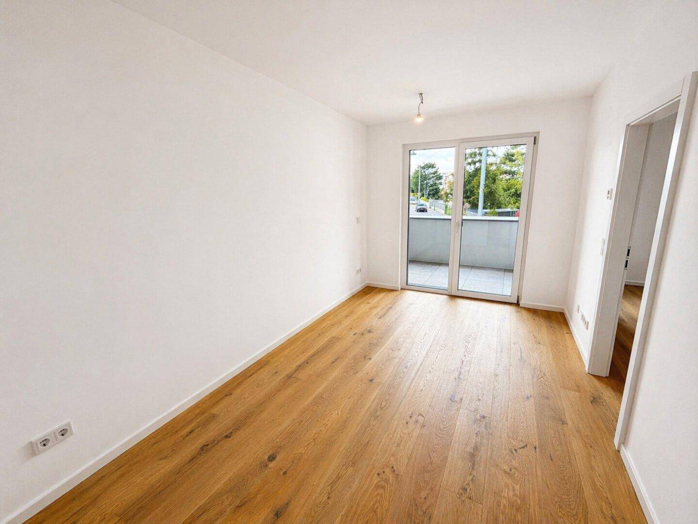 Geräumiger Wohnbereich mit hellem Laminatboden und großen Fenstern zum Balkon.