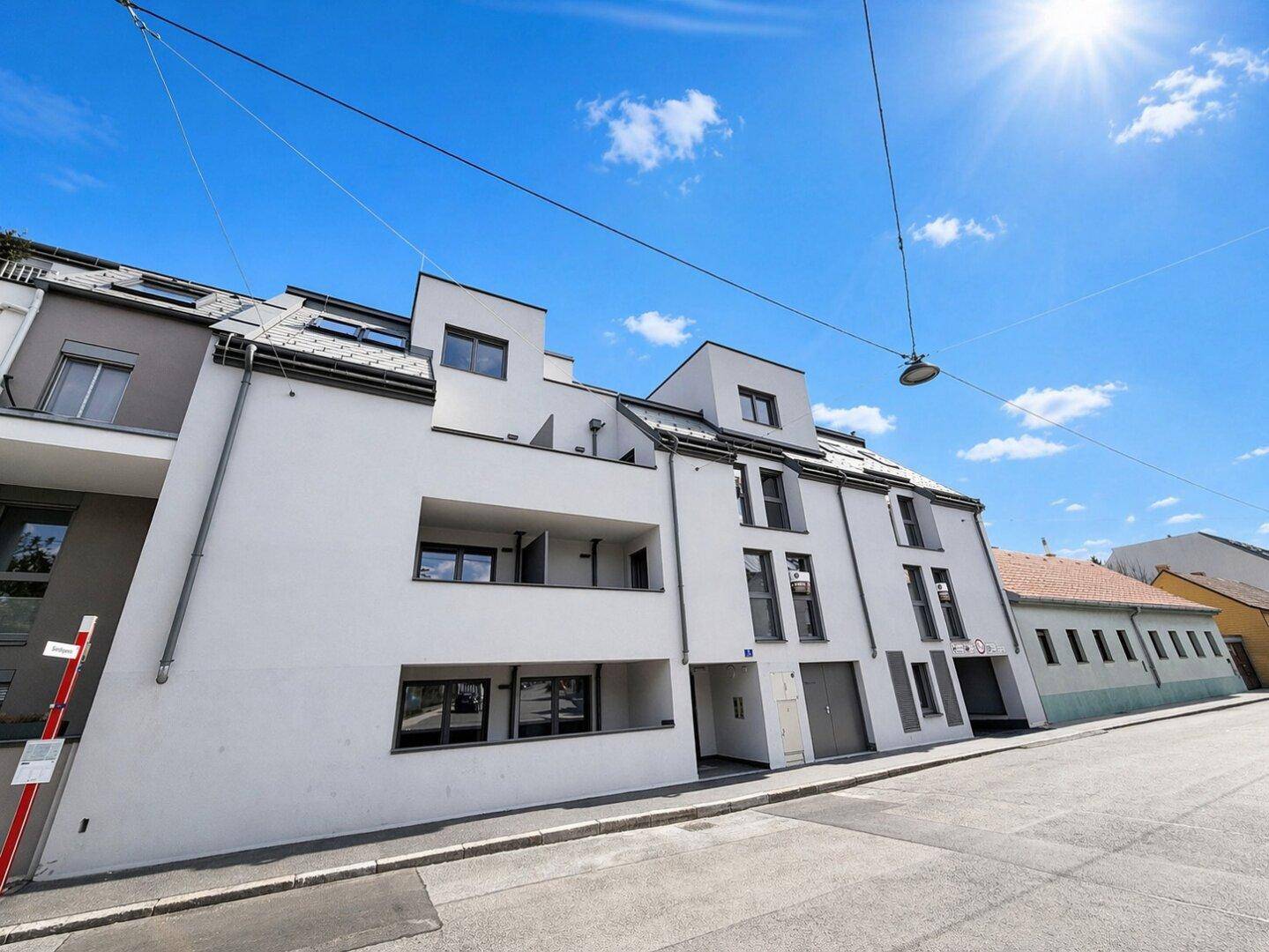 Moderne Wohnanlage mit weißer Fassade und großen Fenstern unter blauem Himmel.