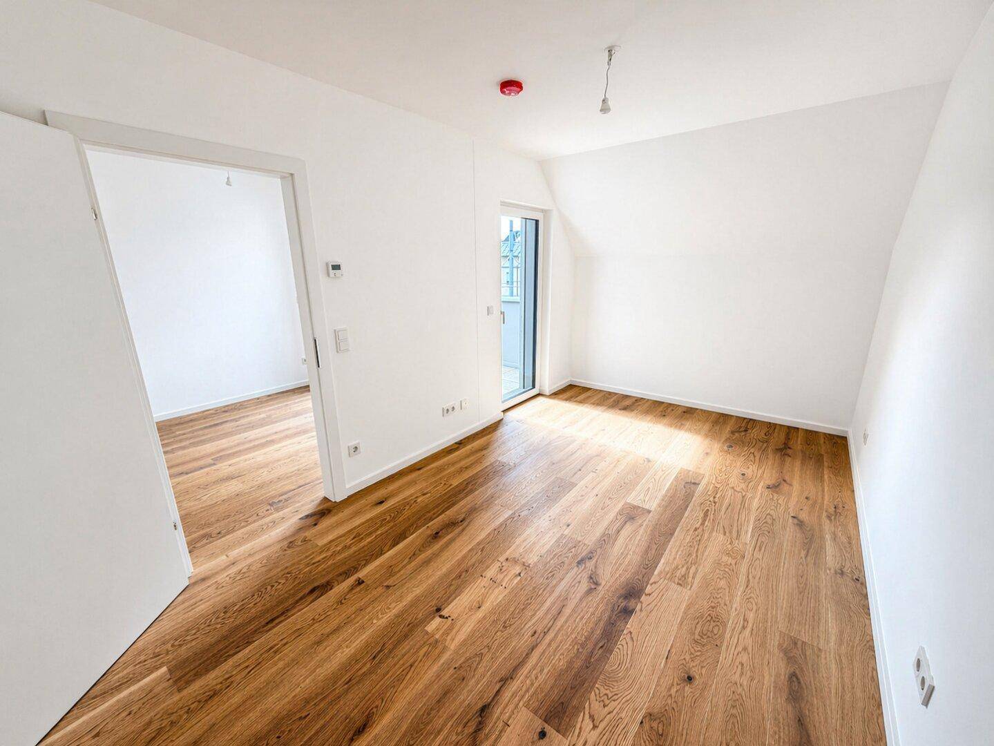Helles Schlafzimmer im Dachgeschoss mit Holzboden und Zugang zu einem kleinen Außenbereich.