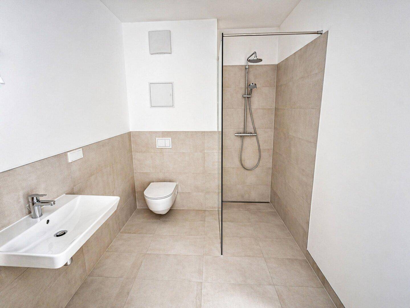 Modernes Badezimmer mit beigefarbenen Fliesen, wandhängendem WC und einer geräumigen begehbaren Dusche.