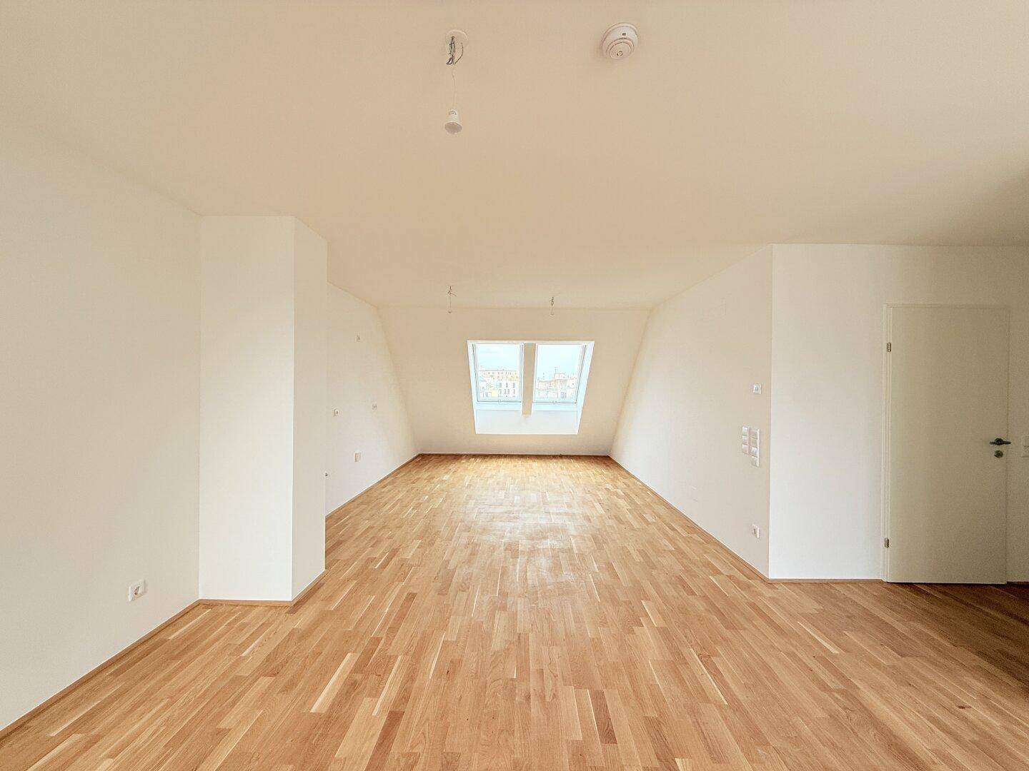 Heller und geräumiger Dachgeschossraum mit Parkettboden und Dachfenster, ideal für offenes Wohnen.