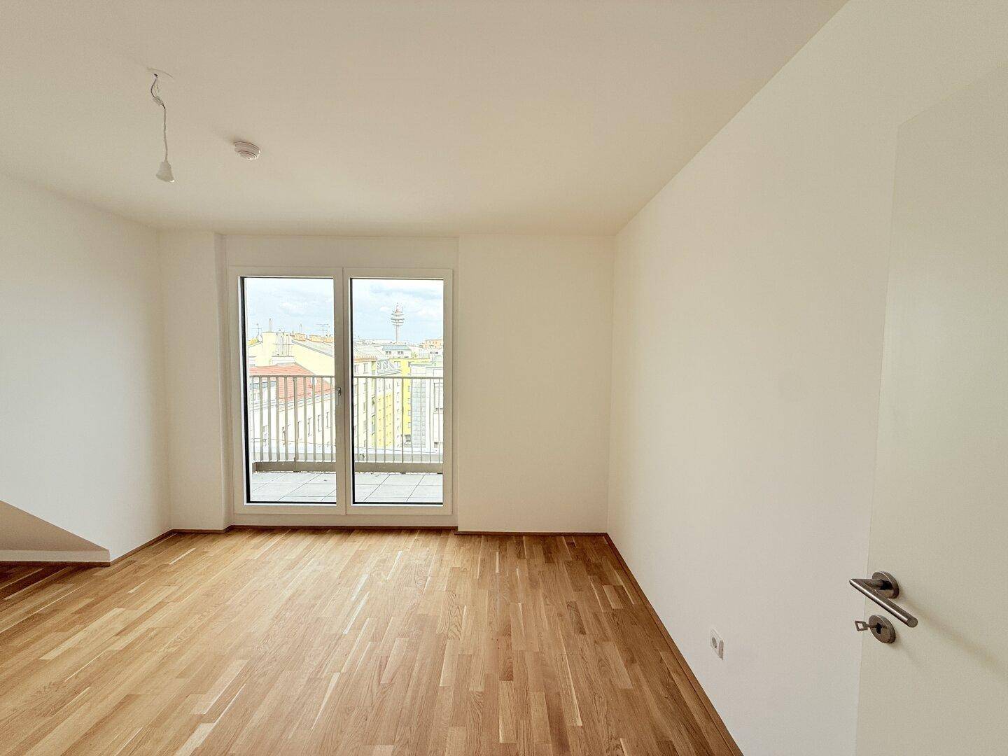 Helles Wohnzimmer mit Parkettboden und großem Fenster mit Zugang zu einem Balkon.