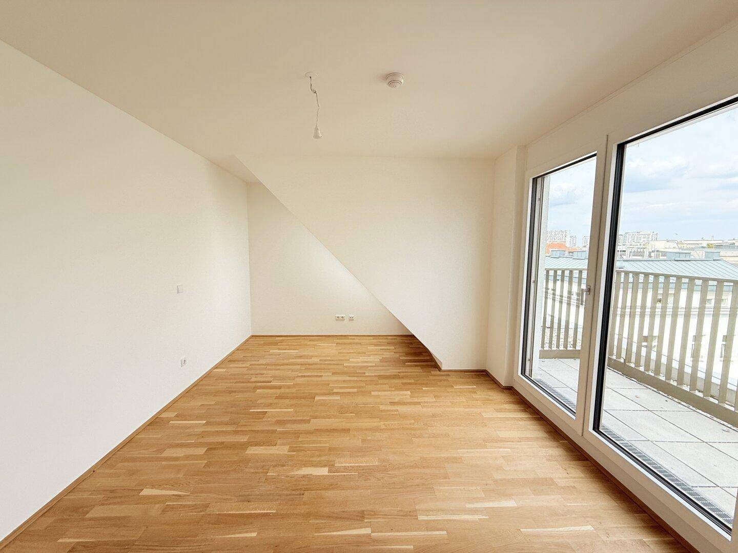 Lichtdurchflutetes Zimmer im Dachgeschoss mit Parkettboden, großen Fenstern und schräger Decke.
