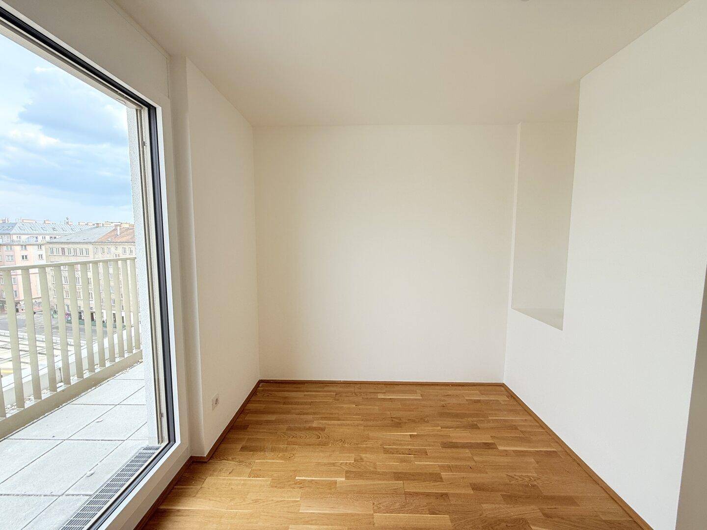 Helles Zimmer mit Parkettboden und großem Fenster, bietet viel Tageslicht und eine Nische.