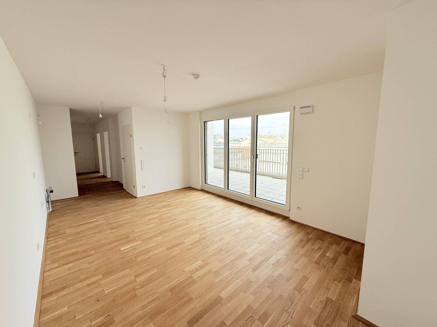 Großer Wohnbereich mit Parkettboden und breiter Fensterfront, bietet Zugang zu einer Terrasse.