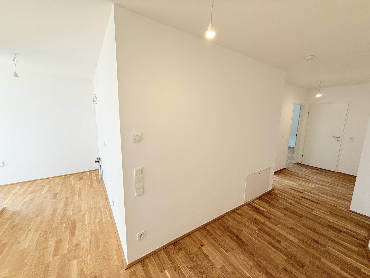 Moderner Flur mit hellem Parkettboden und sauberen weißen Wänden in einem Neubau.