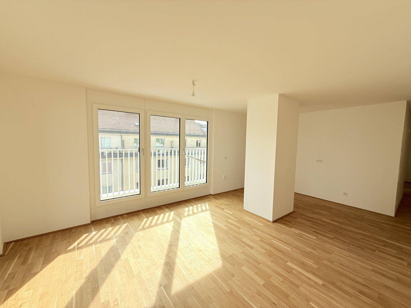 Helles Wohnzimmer mit Parkettboden und großen Fenstern, die viel Sonnenlicht hereinlassen.