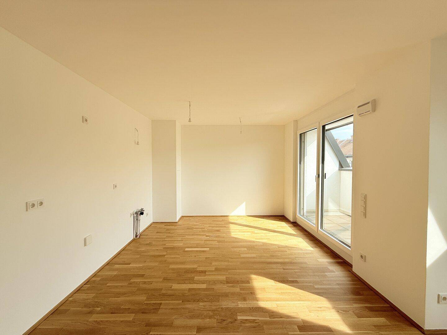 Lichtdurchfluteter Wohnbereich mit Holzboden und Zugang zu einem Balkon.