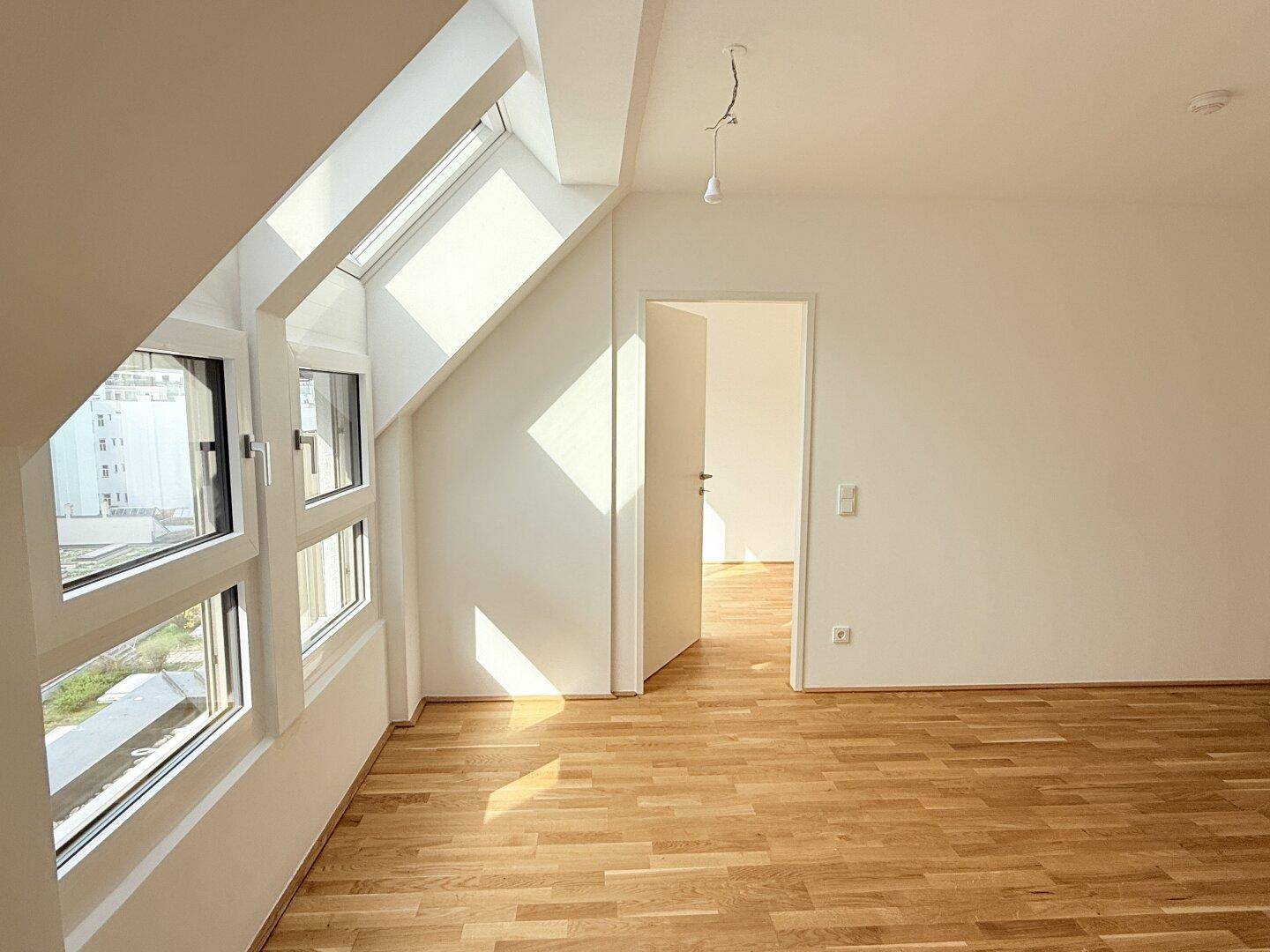 Lichtdurchfluteter Wohnbereich mit Holzparkettboden, weißen Wänden und schrägen Dachfenstern.