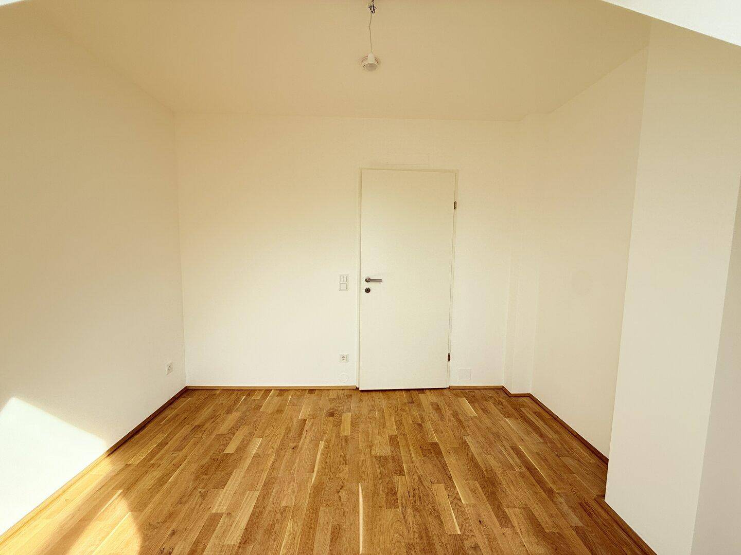 Geräumiges Zimmer im Dachgeschoss mit Holzboden und weißer Tür, bereit zur individuellen Gestaltung.