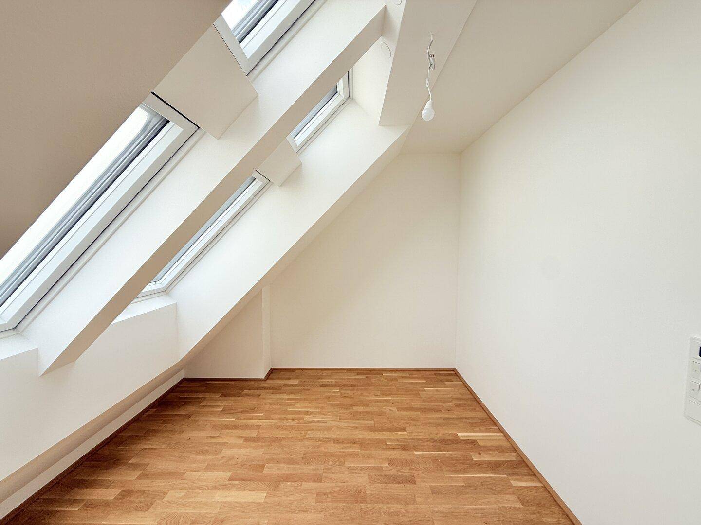 Geräumiges Dachgeschosszimmer mit Holzboden und schrägen Wänden, bietet viel Potenzial für Einrichtung.