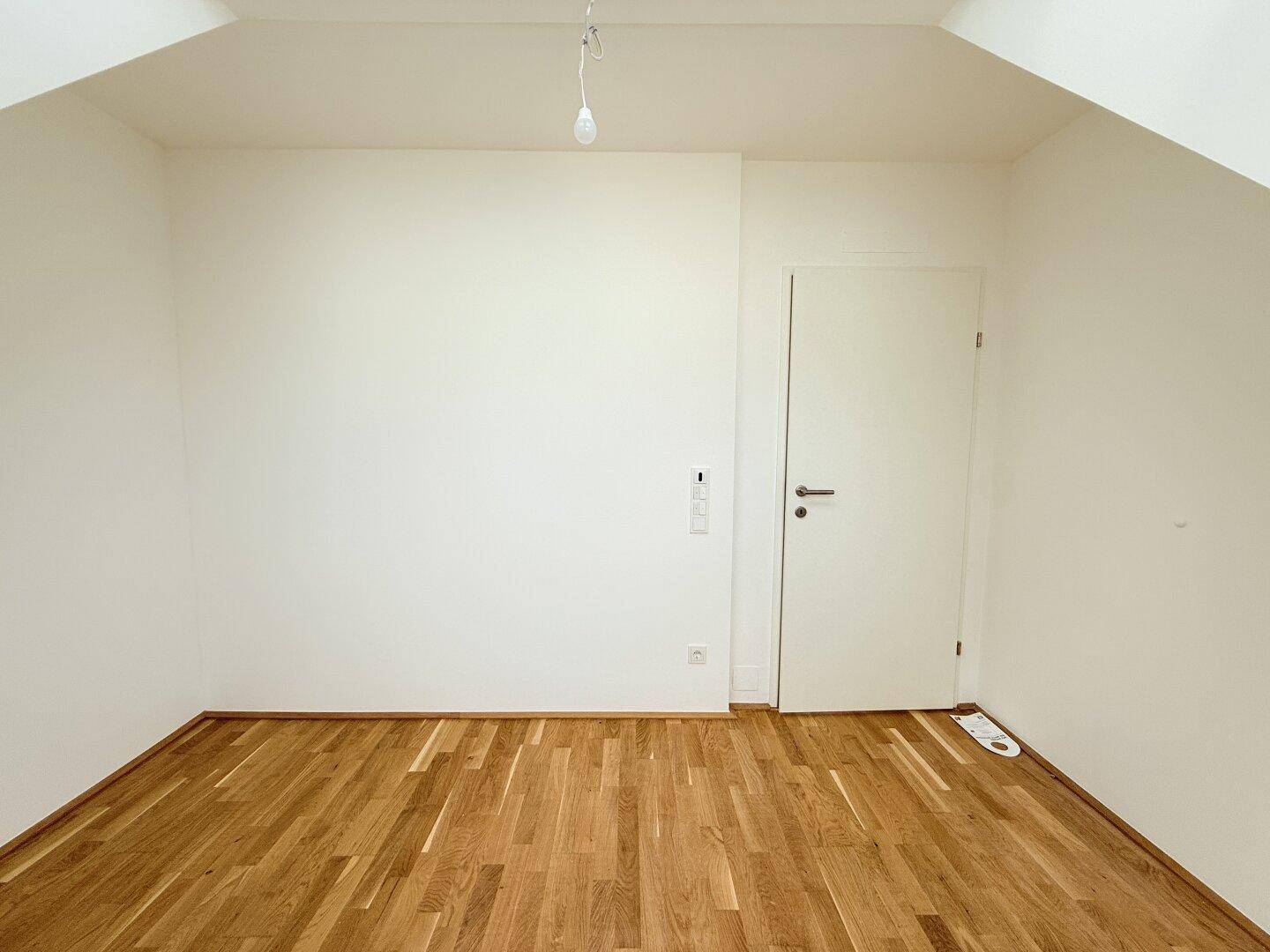 Helles Dachgeschosszimmer mit Holzboden und weißer Tür, ideal für ein Schlaf- oder Arbeitszimmer.