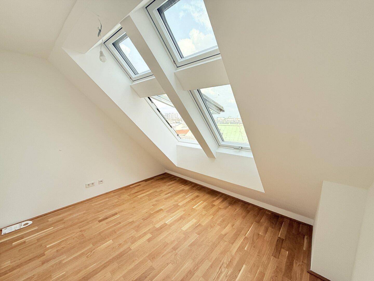 Lichtdurchflutetes Dachgeschosszimmer mit zwei großen Dachfenstern und Holzboden, bietet weite Ausblicke.