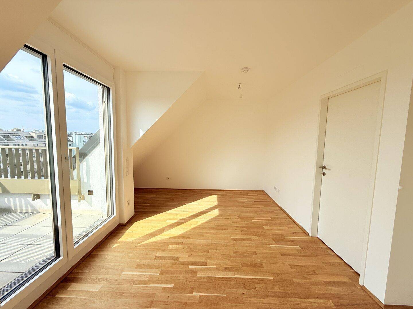 Helles Dachgeschosszimmer mit Holzboden und Zugang zur Terrasse, bietet viel Sonnenlicht.