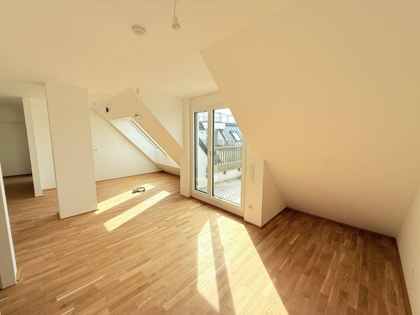 Geräumiger Dachgeschossraum mit Holzboden und Terrassenzugang, bietet eine offene Wohnatmosphäre.