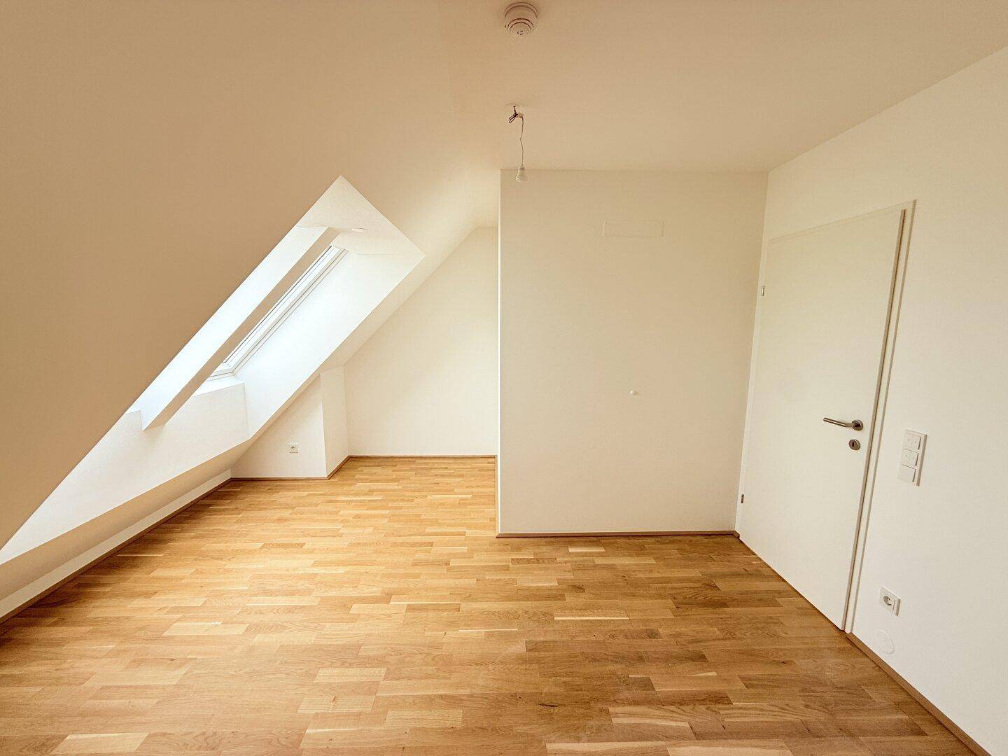 Geräumiges Dachgeschosszimmer mit Holzboden und schrägem Dachfenster, bietet viel Platz.