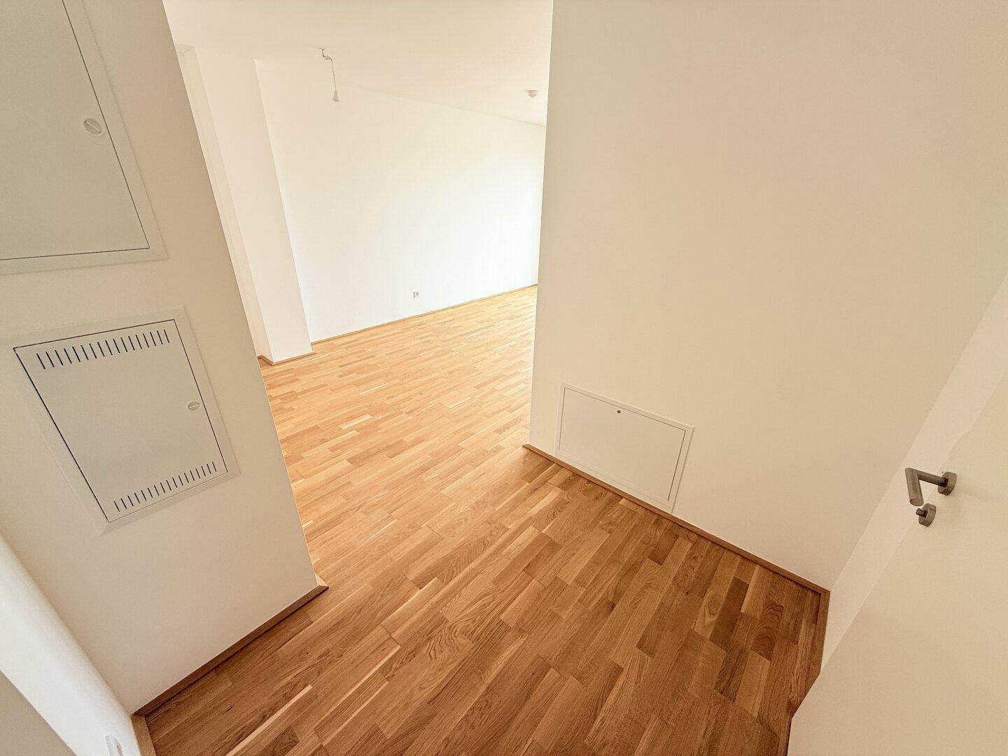 Flur mit hellem Holzboden, der in einen offenen Wohnbereich führt.