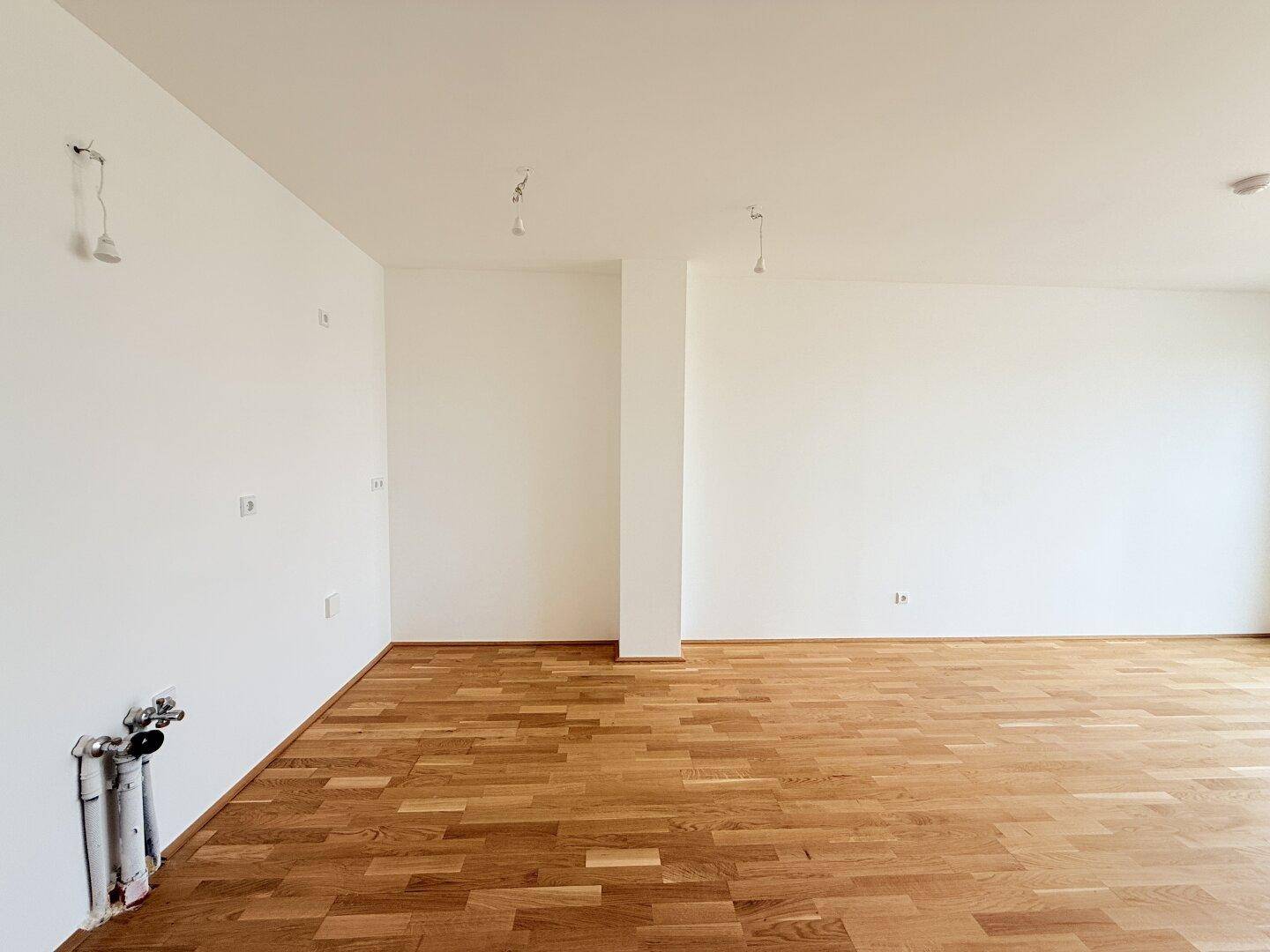 Geräumiger, leerer Wohnbereich mit hellem Holzboden und weißen Wänden.