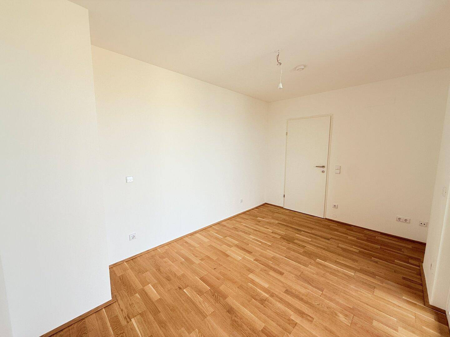 Helles Zimmer mit Holzboden und weiß gestrichenen Wänden, bereit zur individuellen Gestaltung.