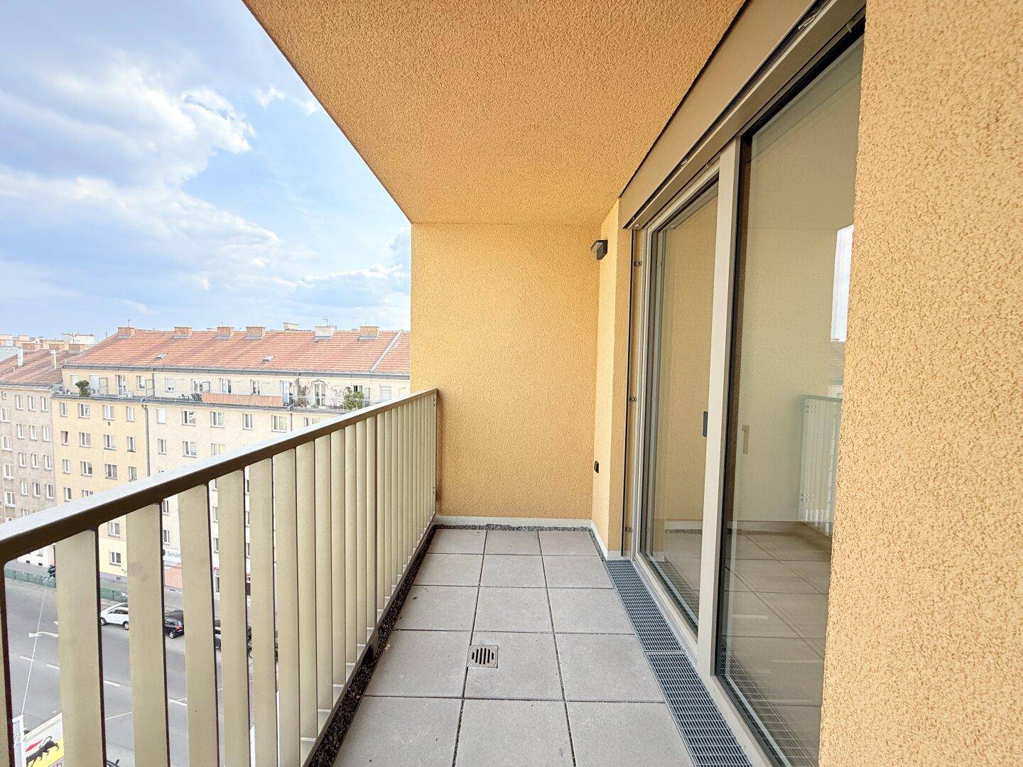 Langer Balkon mit Fliesenboden und Blick auf die Straße und Gebäude.