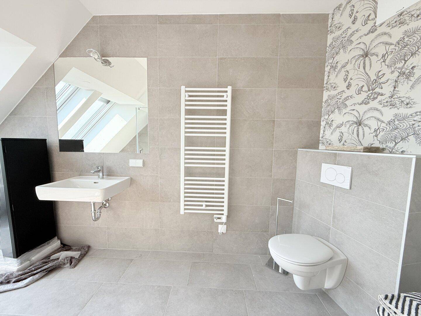 Modernes Badezimmer mit grauen Fliesen, Waschbecken, Toilette und beheiztem Handtuchhalter.