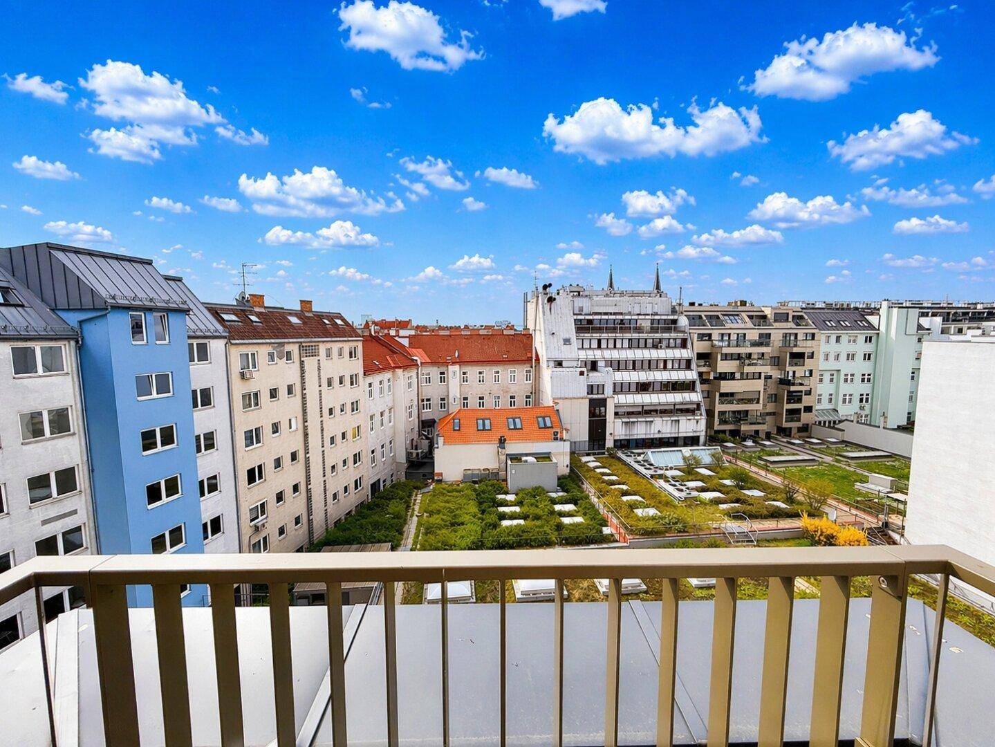 Blick vom Balkon auf die umliegenden Gebäude und begrünte Dächer unter klarem Himmel.