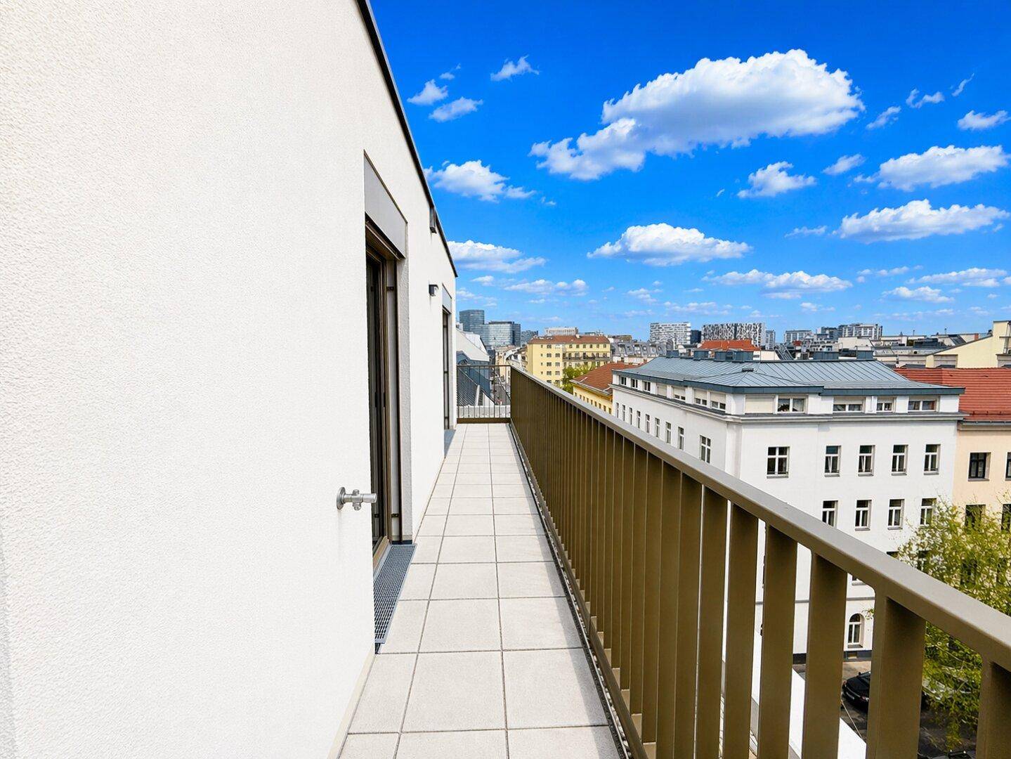 Langer Balkon mit Fliesenboden und Metallgeländer, bietet einen weiten Blick über die Stadt.