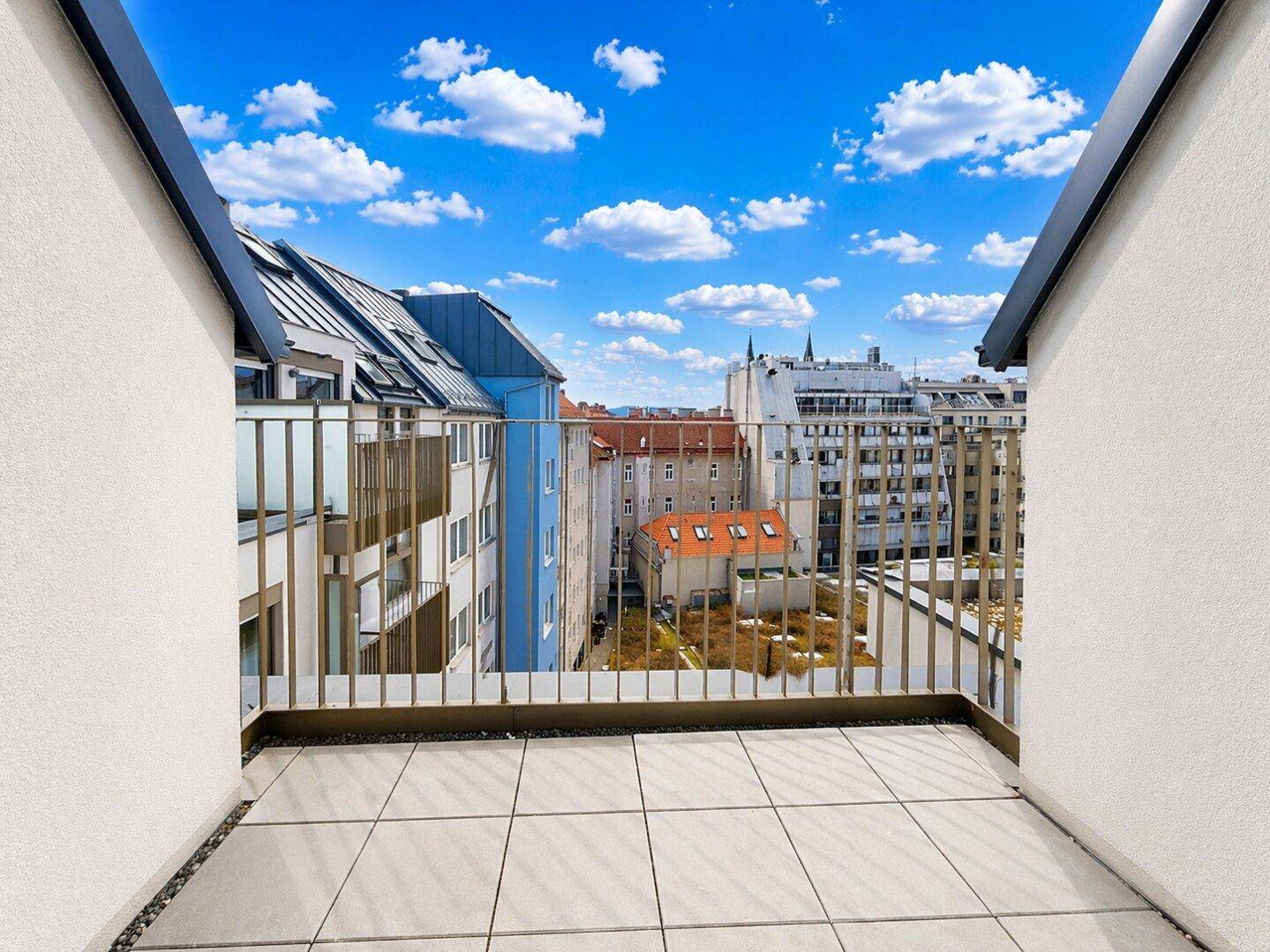 Heller Balkon mit Fliesenboden und weitem Blick über die Dächer der Stadt an einem sonnigen Tag.