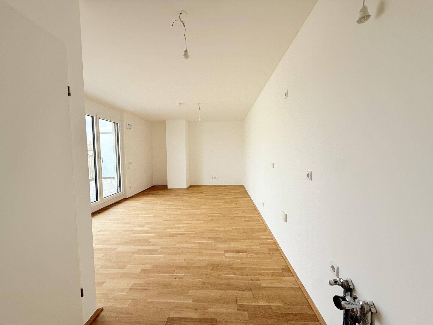 Großer offener Raum mit Parkettboden und Anschlüssen für eine Küche oder Wohnbereich.
