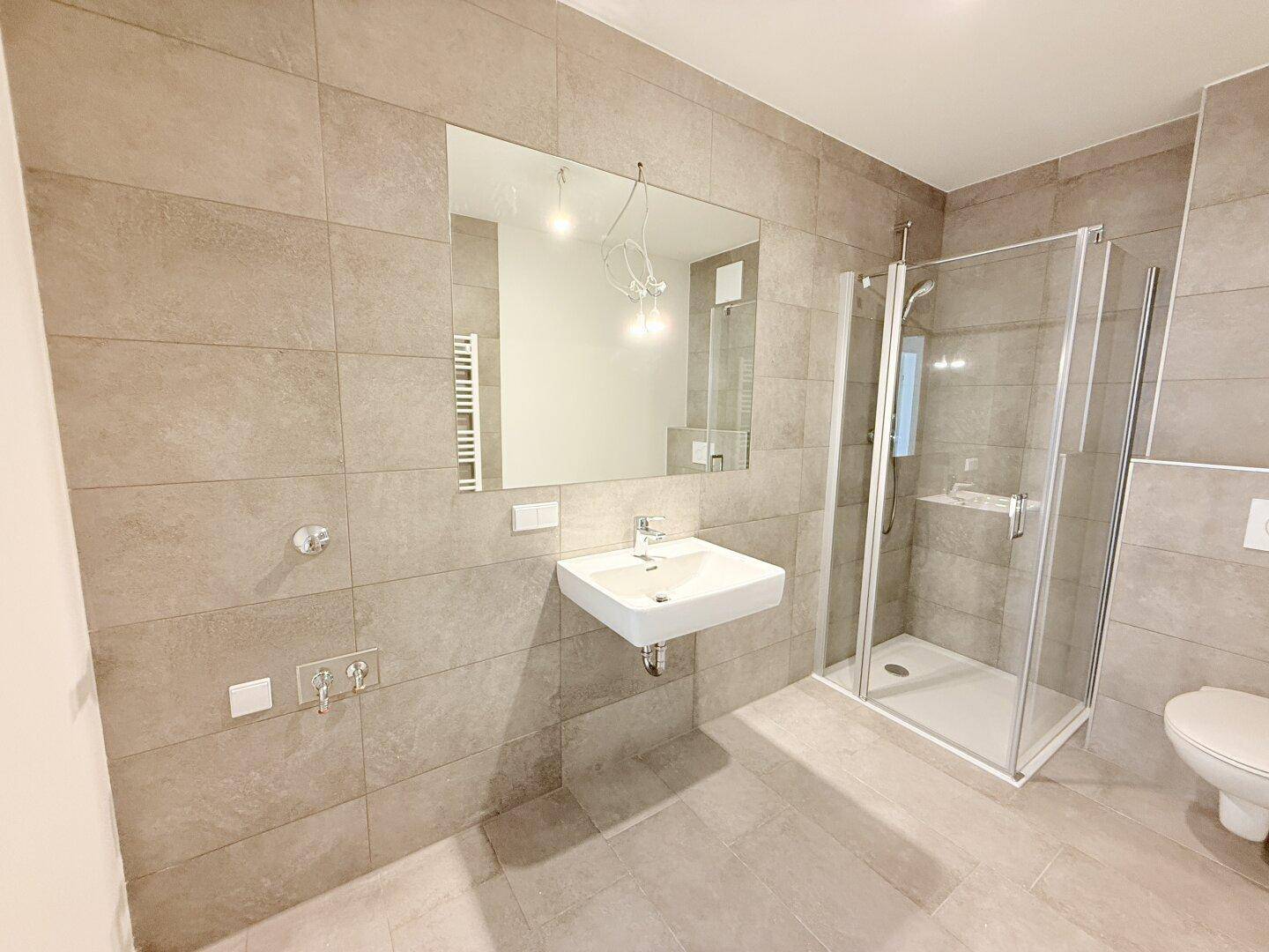 Helles Badezimmer mit großer Dusche, modernem Waschbecken und Fliesenboden.