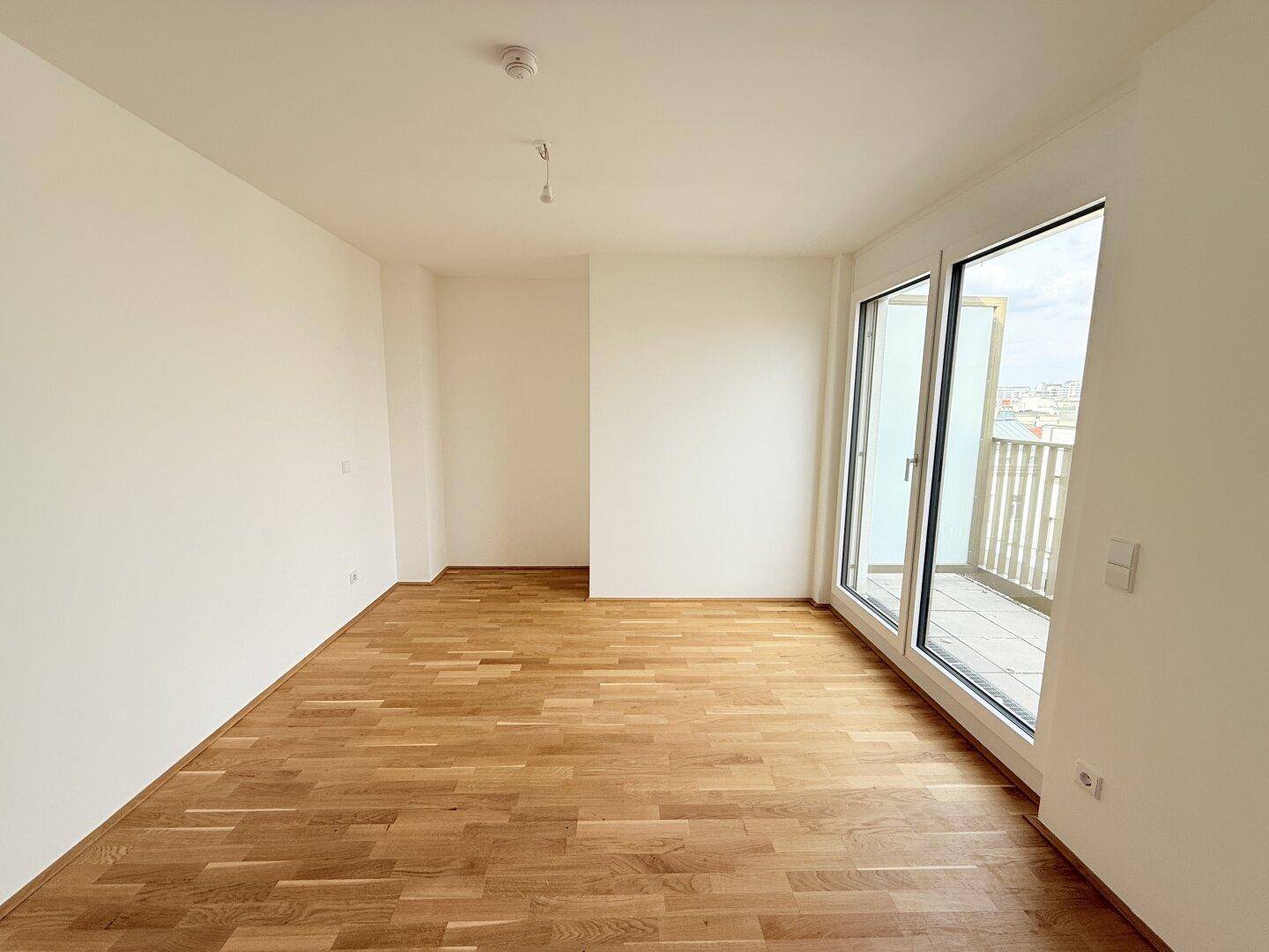 Helles und geräumiges Zimmer mit Holzparkettboden und bodentiefen Fenstern, die auf einen Balkon führen.