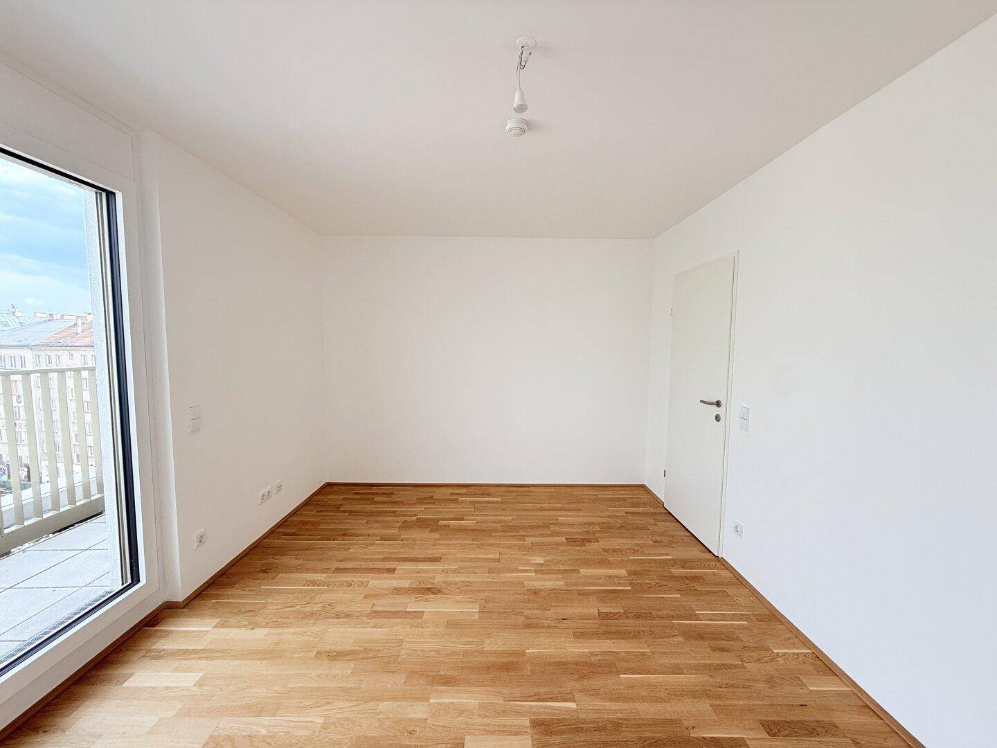 Leeres Zimmer mit warmem Holzparkettboden und weißen Wänden, bereit für individuelle Gestaltung.