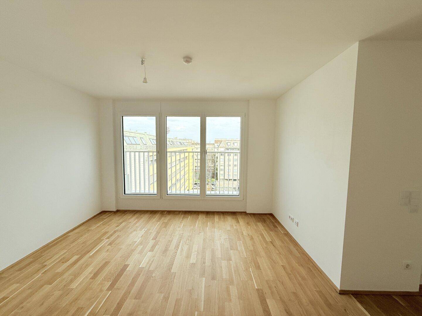 Helles Zimmer mit Holzparkettboden und einer Reihe von drei großen Fenstern, die viel Licht hereinlassen.