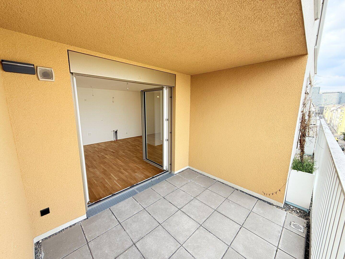 Überdachte Loggia mit Fliesenboden und Zugang zu einem hellen Innenraum durch eine große Glastür.